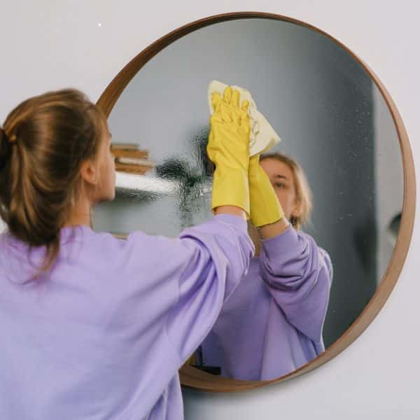 A deep house cleaners cleaning a mirror in a client home.